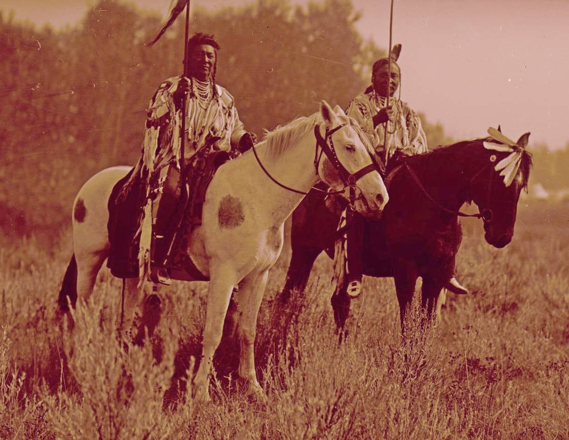 Mounted Crow warriors wearing war shirts. A photograph by Richard Throssel.
